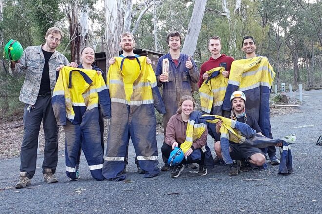 Eight people holding muddy overalls