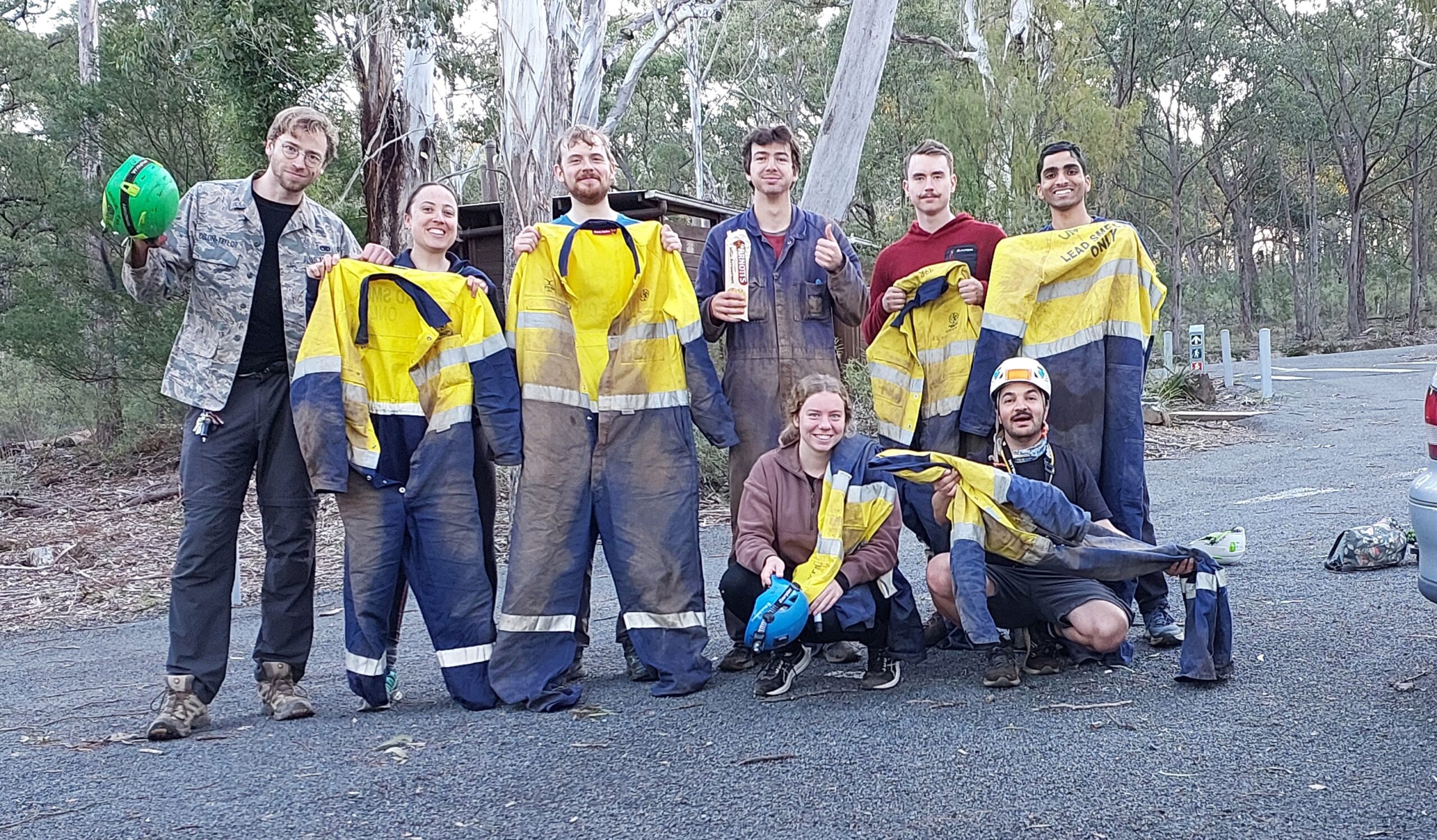 Eight people holding muddy overalls